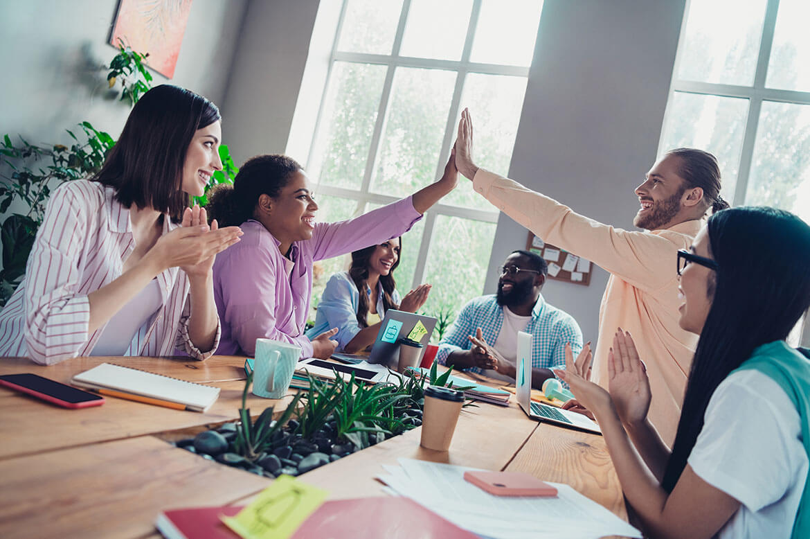 A group of teachers are sitting at a table. 2 teachers giving each other a high five.