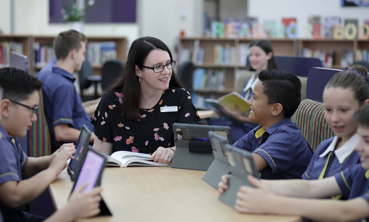 Teacher seated at a table with students who are using Gizmos on Ipads.